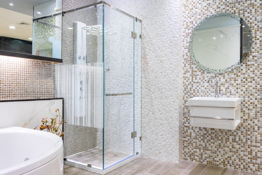 Spacious and bright modern bathroom interior with white walls, a shower cabin with glass wall, a toilet and faucet sink