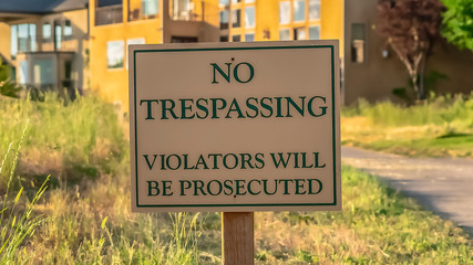 Panorama frame Close up of No Trespassing sign post beside a paved road that leads to houses