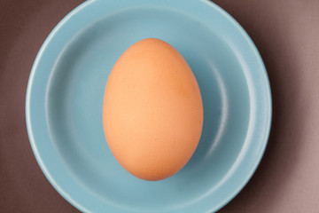 One raw egg on blue plate on brown background from top view with space for copy.