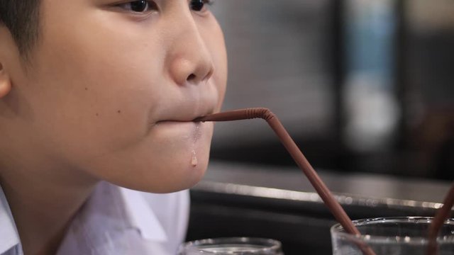 Asian boy drinking water from straw in restaurant.