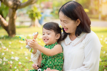 Asian Grandmother and granddaughter sitting and playing hand puppet together in the garden.Happy Asian family conception.