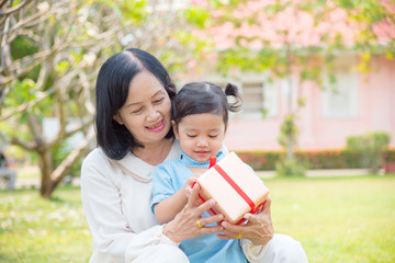 Asian Grandmother giving birthday gift for granddaughter in the garden.Happy Asian family conception.