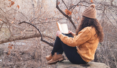 Girl reading a book in the autumn park.