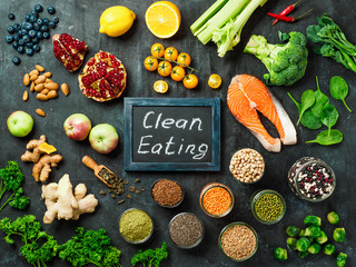Clean-Eating-Konzept. Auswahl an Lebensmittelzutaten und Tafel mit sauberen Essenswörtern auf dunklem Hintergrund. Ansicht von oben oder flach liegend.