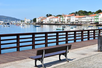 Fototapeta na wymiar Small fishing village with boardwalk and wooden bench. Blue sky, sunny day, Mugardos, Spain.