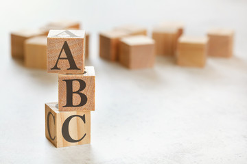 Three wooden cubes with letters ABC (means Always be Closing), on white table, more in background,...