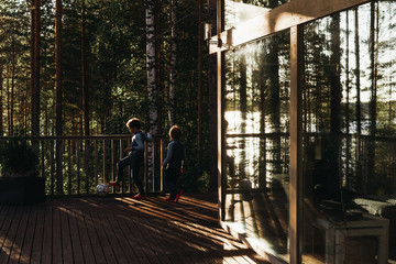 Children play ball on the wooden veranda of a Scandinavian house in the Northern green forest