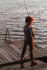 A young boy is fishing on a wooden pier at sunset