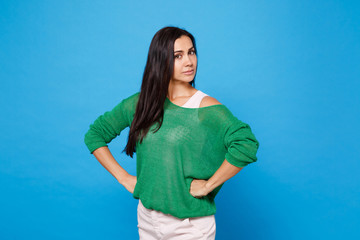 Portrait of strict young woman in green casual clothes looking camera, stand with arms akimbo on...