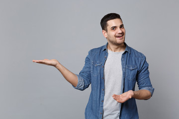 Handsome stylish unshaven young man in denim jeans shirt posing isolated on grey wall background studio portrait. People sincere emotions lifestyle concept. Mock up copy space. Pointing on copy space.