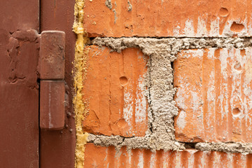 A close up of an old red brick wall and a band of a brown painted metal garage door