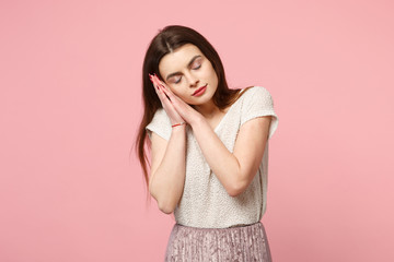Relaxed young woman in casual light clothes posing isolated on pastel pink wall background, studio portrait. People lifestyle concept. Mock up copy space. Sleeping with folded hands under cheek.