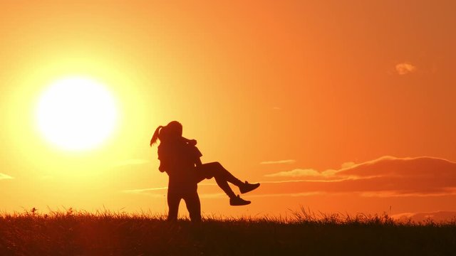 Silhouette of happy couple in love at sunset. boyfriend carrying and spinning his girlfriend.