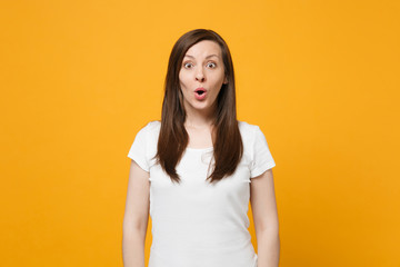 Portrait of shocked young woman in white casual clothes keeping mouth open, looking camera isolated on bright yellow orange wall background in studio. People lifestyle concept. Mock up copy space.