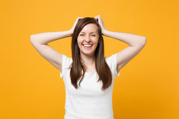 Portrait of cheerful young woman in white casual clothes looking camera, putting hands on head isolated on bright yellow orange wall background in studio. People lifestyle concept. Mock up copy space.