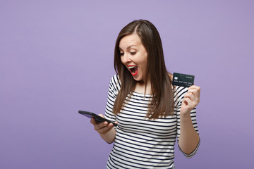 Fototapeta premium Young brunette woman girl in casual striped clothes posing isolated on violet purple background studio portrait. People lifestyle concept. Mock up copy space. Hold in hand credit bank card cellphone.