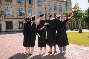 Graduates standing next to each other in front of university.