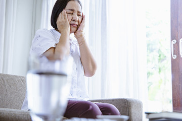 old age, health problem, vision and people concept - close up of Asian senior woman  sitting on sofa and having headache at home.She may had Headache Symptoms.She looks pain  and sick