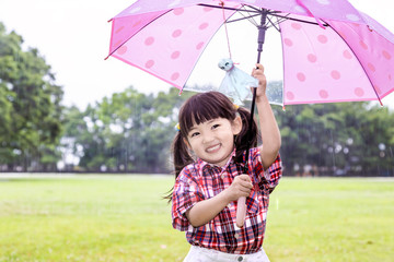 雨の公園で傘を差しカメラ目線の幼い女の子。