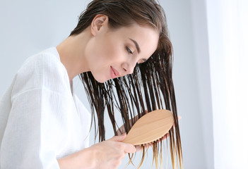 Beautiful young woman brushing hair after washing at home