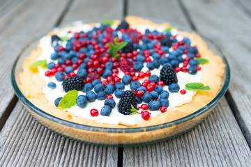Tart with fresh blueberries, raspberries, blackberries, red currants and whipped cream decorated with mint leaves. View from above