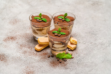 Classic tiramisu dessert in a glass cup and savoiardi cookies on concrete background
