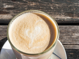 Glass cup of coffee latte with beautiful heart shape, wooden table