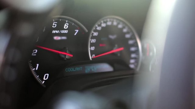 Dashboard speedometer and tachometer of a sports car shooting through the steering wheel. Close-up and selective focus of the tachometer needle
