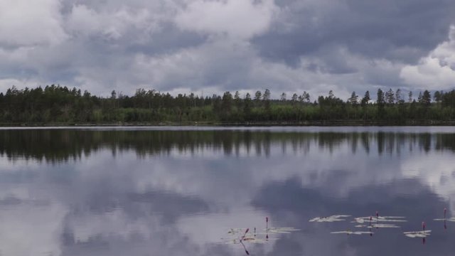 Rainclouds over a Swedish lake inside a forest with the water creating a mirror reflection in the water of the clouds and trees.