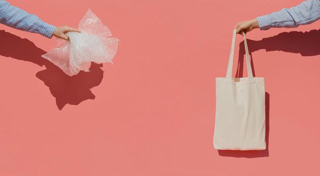 Reusable shopping bag instead of thousands of plastic bags. Eco trend to reduce disposable plastic. Hands on pink background holding plastic bags and cotton shopper bag.