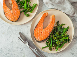 Ready-to-eat grilled salmon steak and greens - baby broccoli or broccolini and spinach on rustic craft plate over gray background. Keto diet dish. Top view or flat lay. Copy space for text or design.