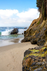 Ocean waves breaking on rocks offshore at Wood's Cove in Laguna Beach, California. Detailed closeup of colorful moss and lichens growing on rugged cliffs in the foreground.