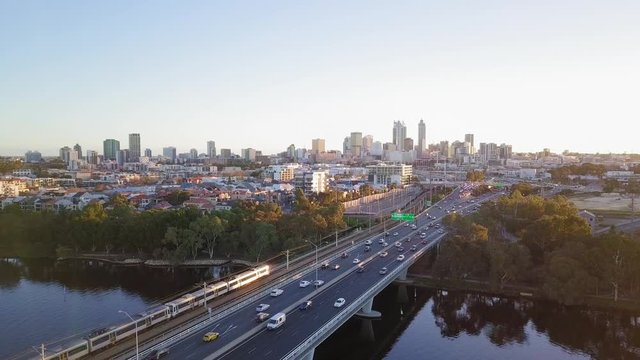 Aerial sideways motion over a bridge leading to Perth City in Western Australia. Cars going thorough the bridge at golden hour with view at the skyline.