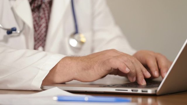 Physician introducing patient medical data on laptop and talking on mobile phone, close up