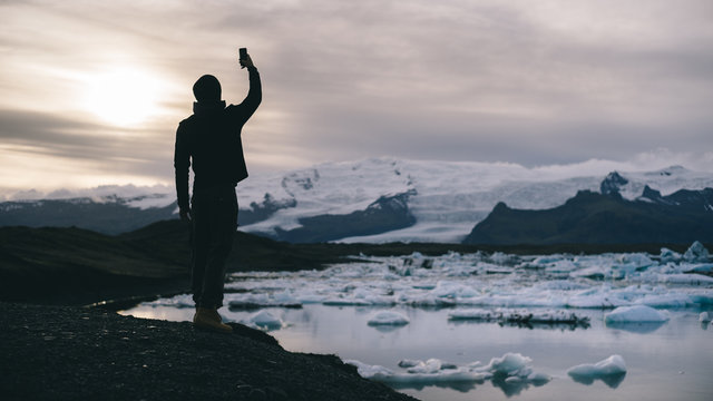 Silhouette of a man taking picture using mobile phone during sunset time at the Jökulsárlón Glacial Lagoon in Iceland