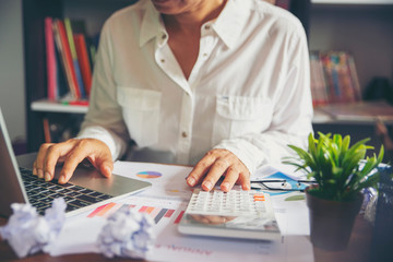Fototapeta premium Annual Report,summary report and paper placed on office desk.Person back view of Asian woman working and planning financial data with laptop.Business woman and planner concept.