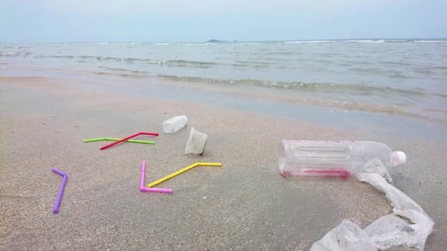 Colorful plastic straws cup bottle bag single use on the sand in the ocean with ocean waves. The people throwing trash carelessly in anywhere not a bin. Environment negligently concept.