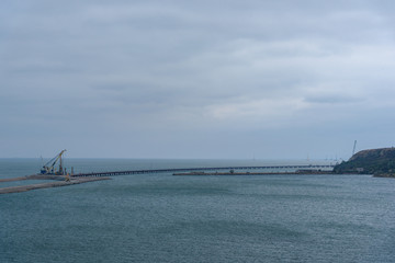 The shore of the Kerch Strait during the construction of the Kerch Bridge in cloudy weather with clouds in the sky.