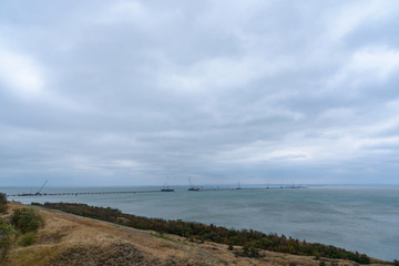 The shore of the Kerch Strait during the construction of the Kerch Bridge in cloudy weather with clouds in the sky. .