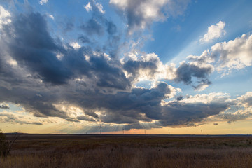 sandy beach in the light of the setting sun with a huge cloud in the sky, wind generators standing in the field.