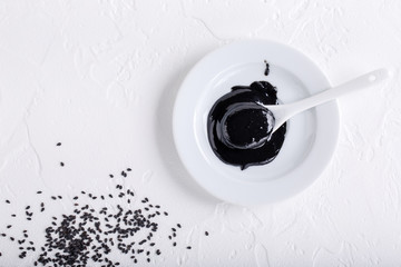 Black tahini sauce and black sesame seeds in bowls on white background. Natural paste made from...