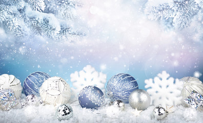 Christmas decorations with blue and white balls, snowflakes in the snow and snow covered fir branches. Copy space.