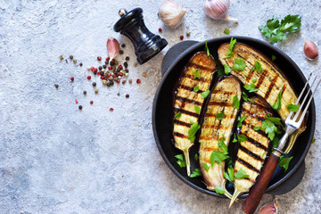 Spicy eggplant grilled in a cast-iron frying pan on a concrete background.