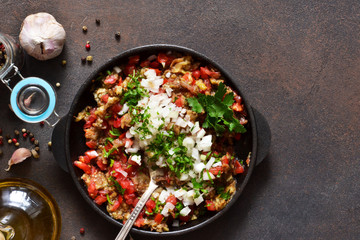 Appetizer with eggplants, tomatoes, onions and spices in a frying pan on a concrete background.
