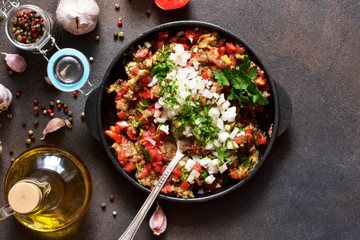 Appetizer with eggplants, tomatoes, onions and spices in a frying pan on a concrete background.