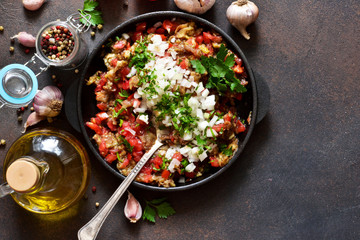 Appetizer with eggplants, tomatoes, onions and spices in a frying pan on a concrete background.