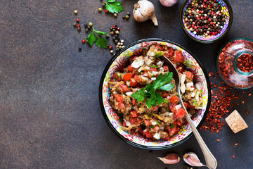Appetizer with eggplants, tomatoes, onions and spices in a frying pan on a concrete background.