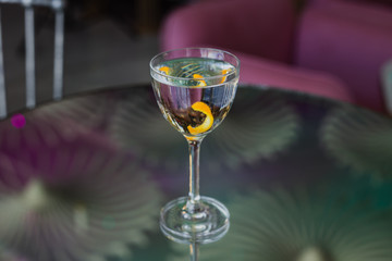 Dry martini cocktail with an orange twist in a nick and nora glass on a glass table with a reflection