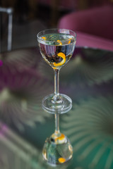 Dry martini cocktail with an orange twist in a nick and nora glass on a glass table with a reflection