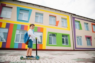 Boy goes to school on a scooter. Children back to school scoote.Childschool riding a scooter. Back to school. Happy children. Happy childhood lifestyle. Student goes to school